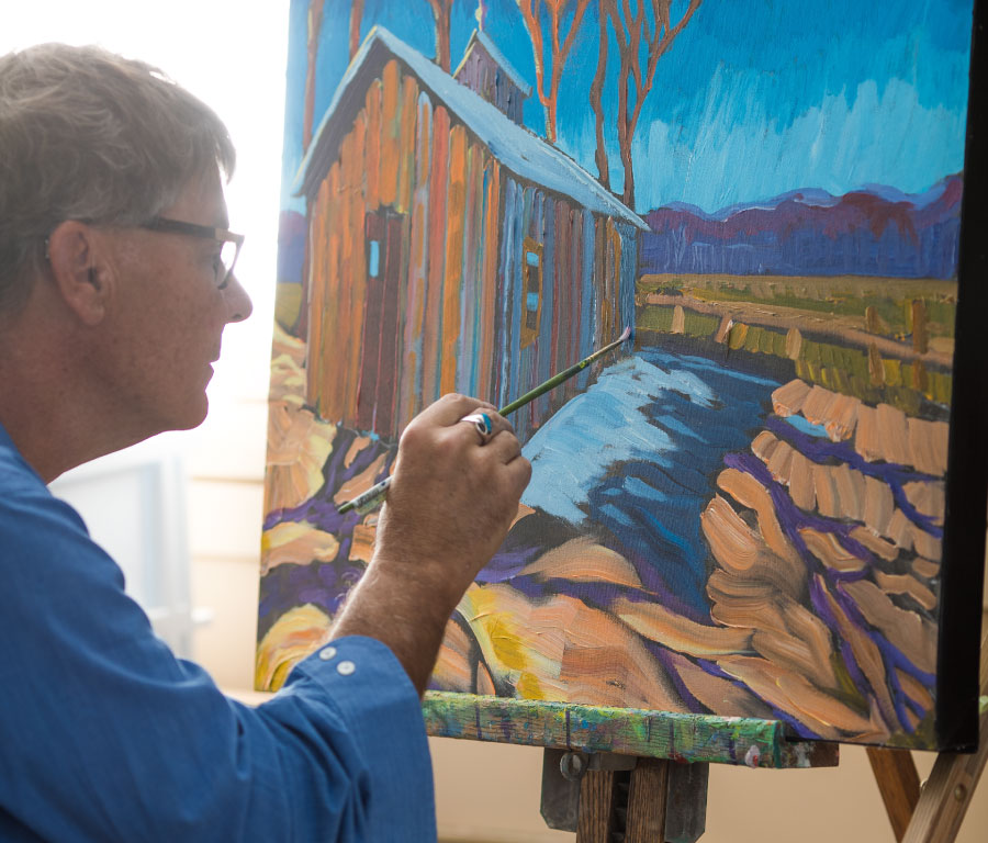 The artist at work, painting a colourful barn and landscape